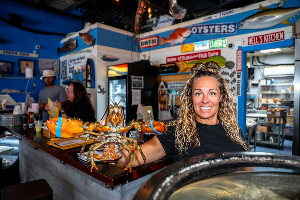 A staff member holding a live lobster over the ice at the counter